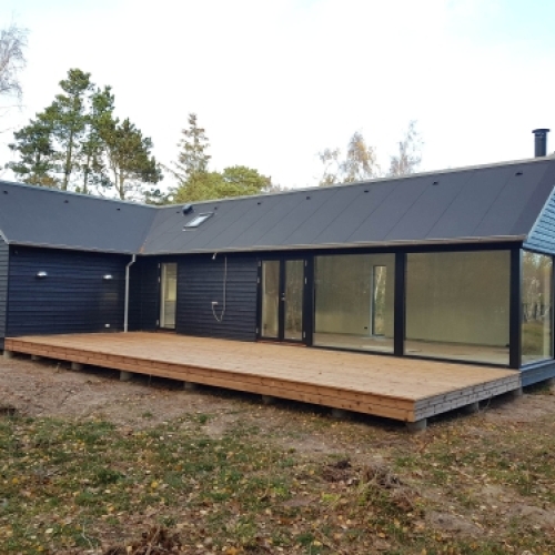 Ny træterrasse ved hus med store vinduespartier og mørk facade
