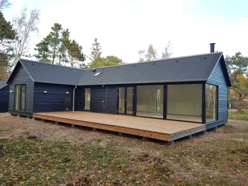 Ny træterrasse ved hus med store vinduespartier og mørk facade